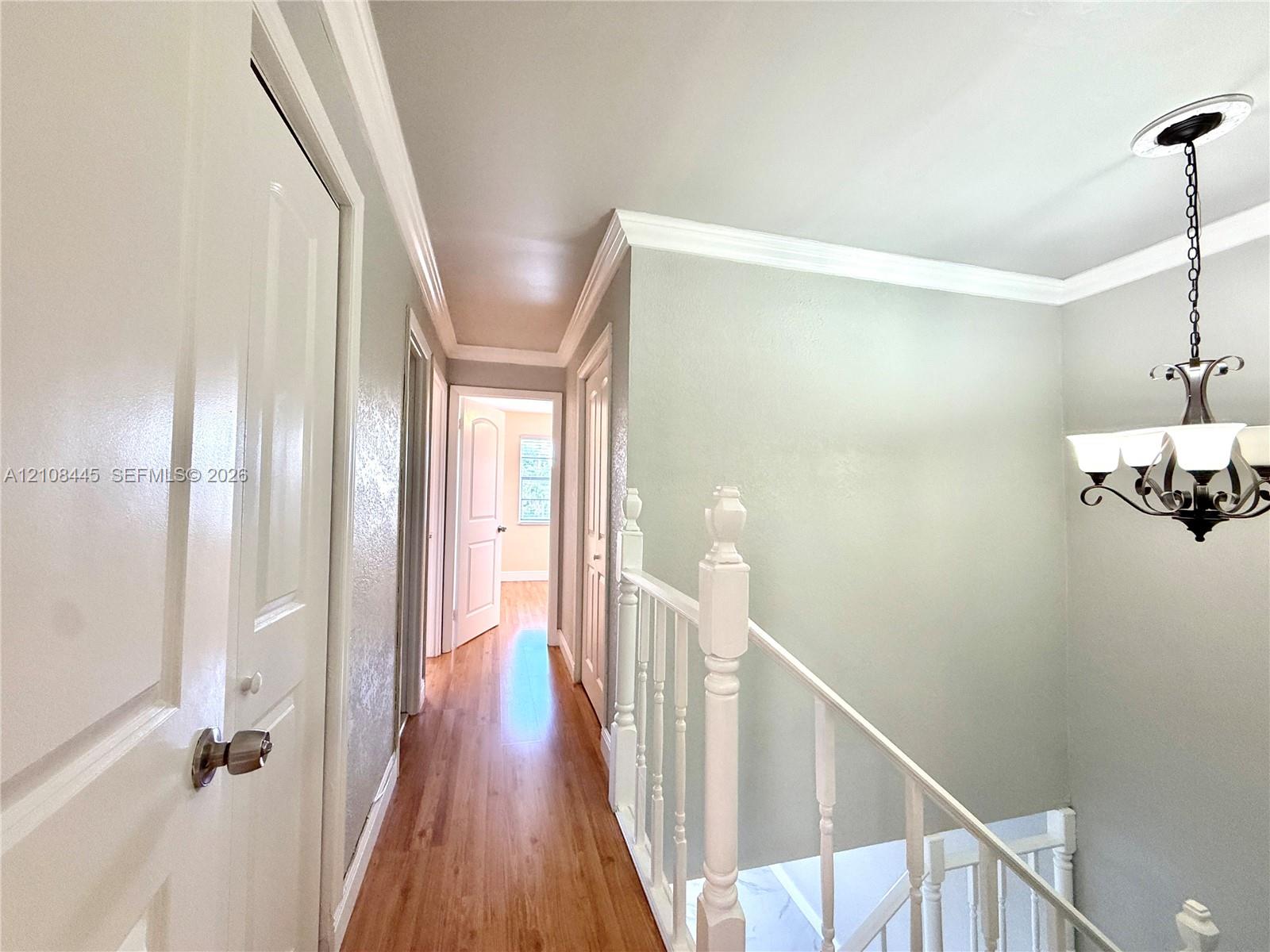 Hallway featuring wood-finish flooring, crown molding, a multi-bulb chandelier.