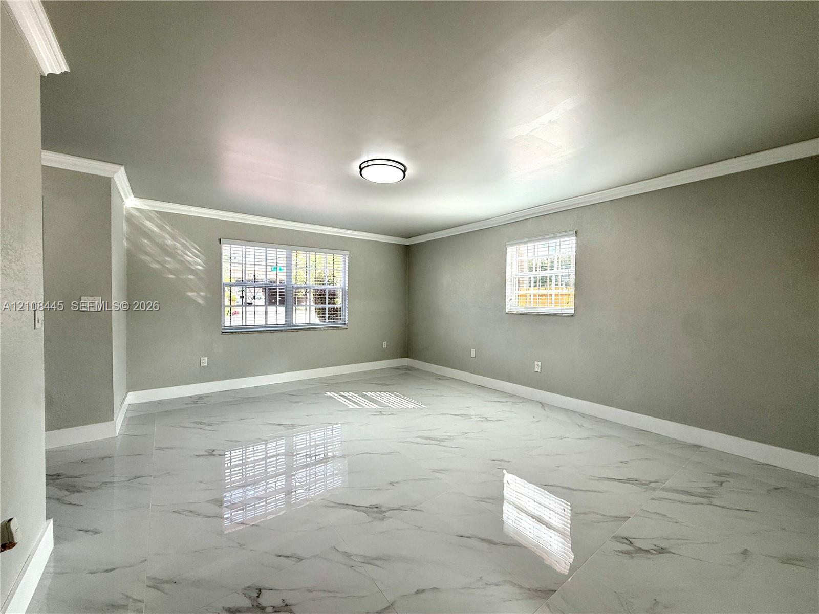 Living Area featuring large-format polished tile flooring, neutral wall tones, crown molding, and dual windows