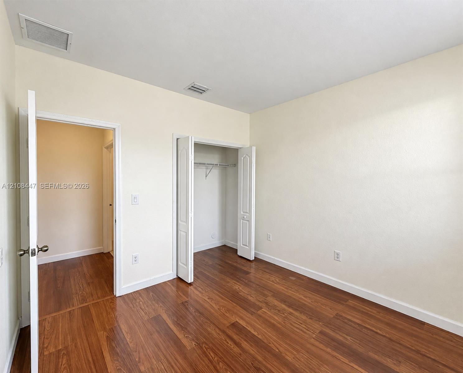 Room featuring wood-finish flooring, neutral wall tones, and a built-in reach-in closet with double-panel doors