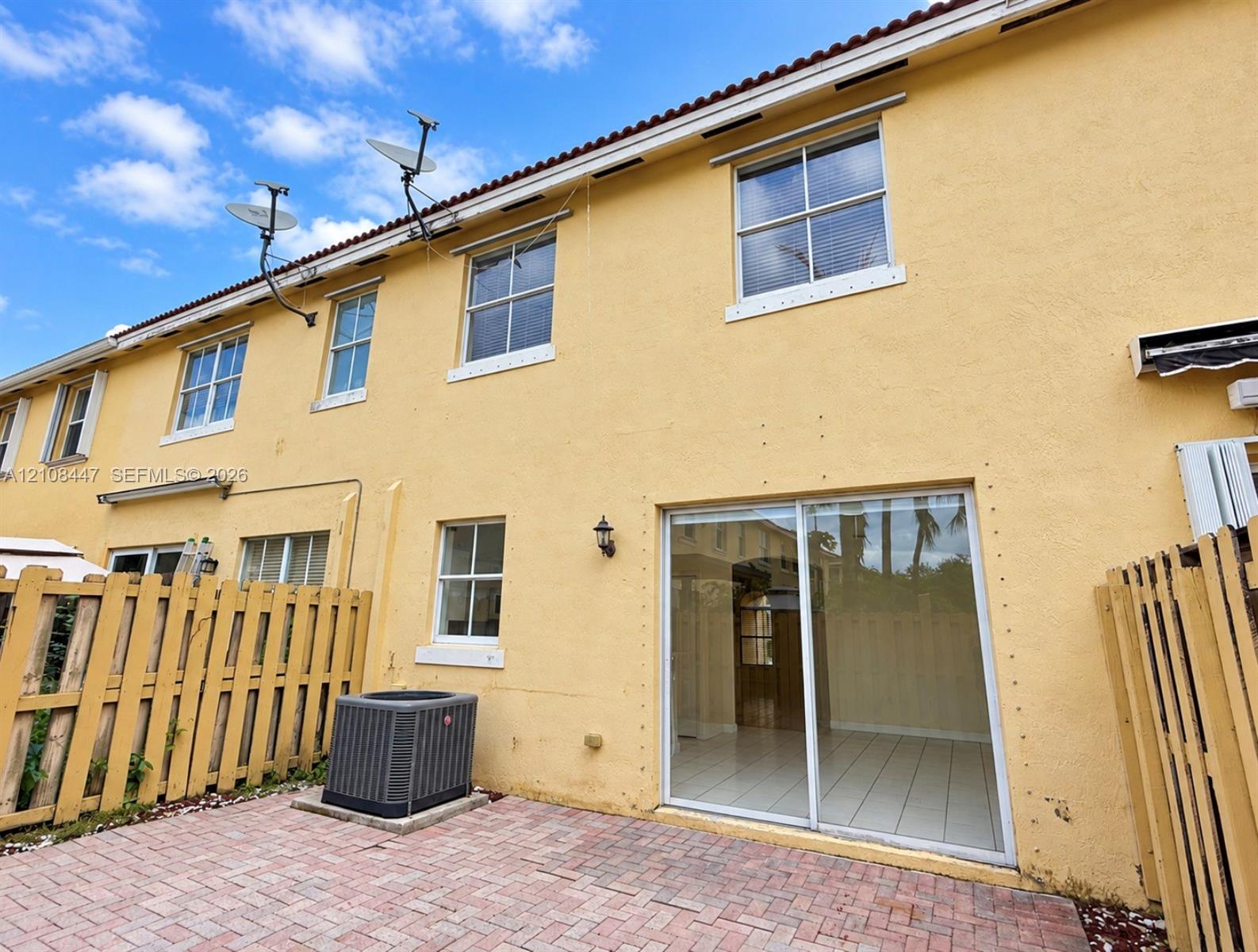 Exterior rear facade featuring a stucco finish, sliding glass patio door, paver patio, and multi-pane windows