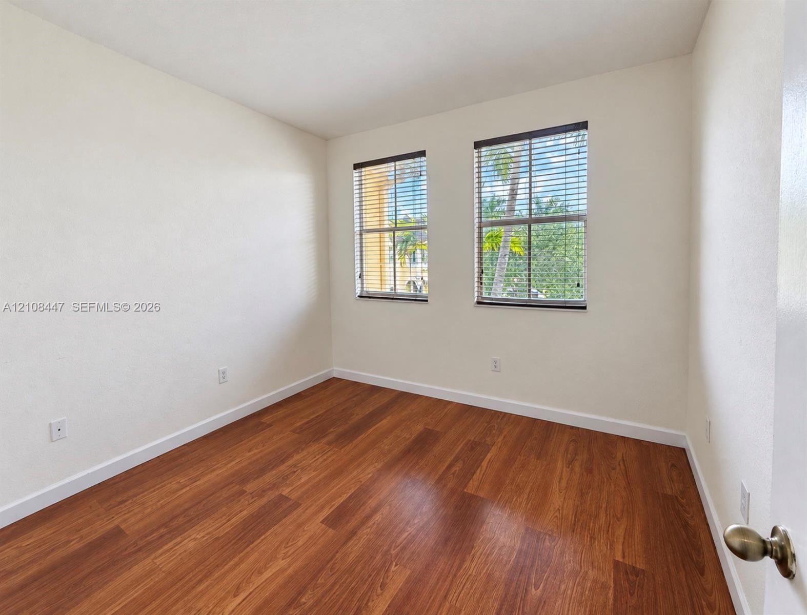 Interior room featuring wood-finish flooring, neutral walls, and two windows with horizontal blinds