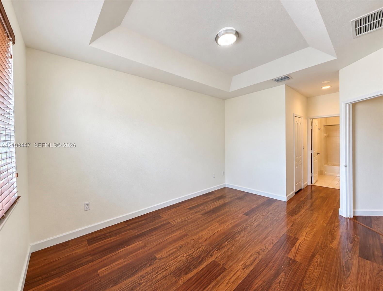 Interior room featuring a tray ceiling, wood-finish flooring, and natural light from window blinds