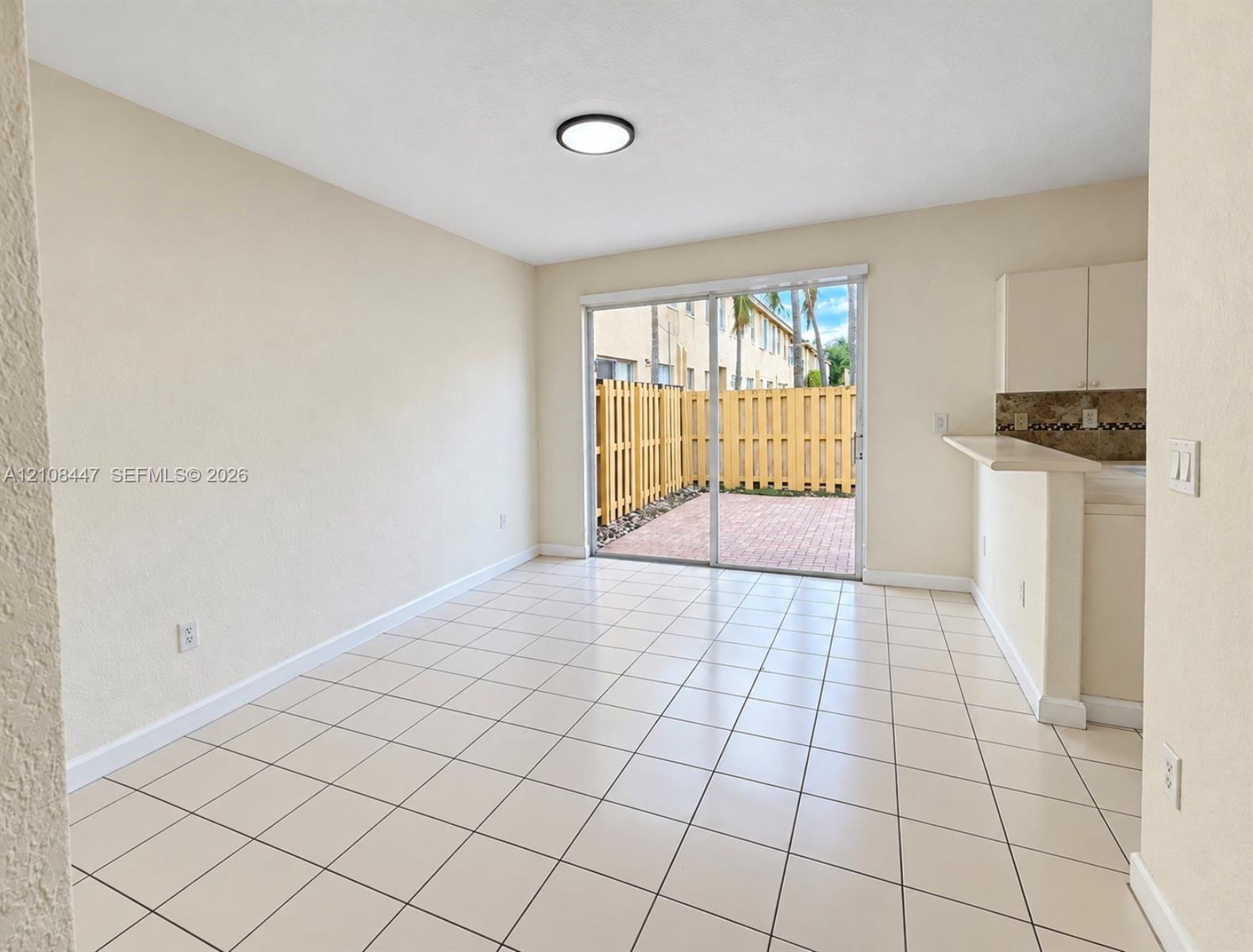 Neutral-toned interior featuring ceramic tile flooring, a breakfast bar, and sliding glass doors opening to a private, fenced brick patio