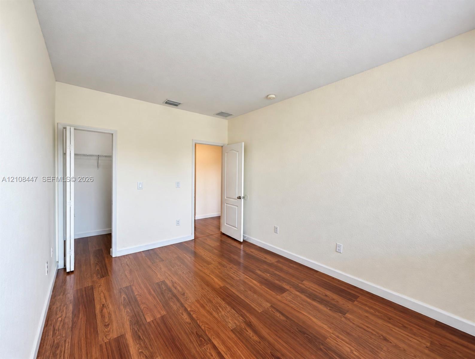 Interior space featuring wood-finish flooring, neutral wall tones, a multi-panel interior door, and a built-in closet with wire shelving