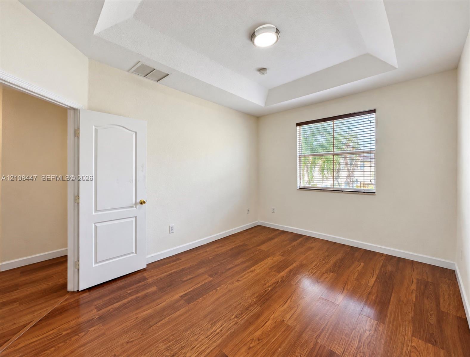 Room featuring a tray ceiling, wood-finish flooring, and a window with horizontal blinds