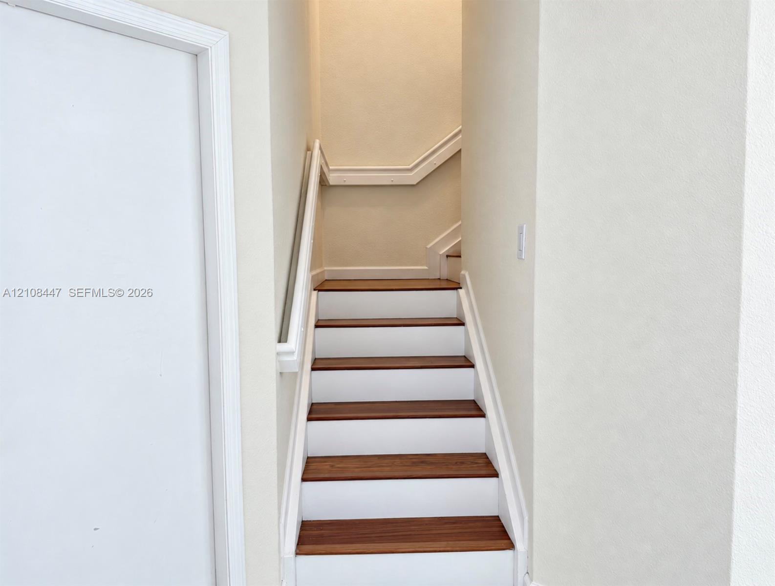 Staircase featuring wood-finish treads, white risers, and a continuous wall-mounted handrail