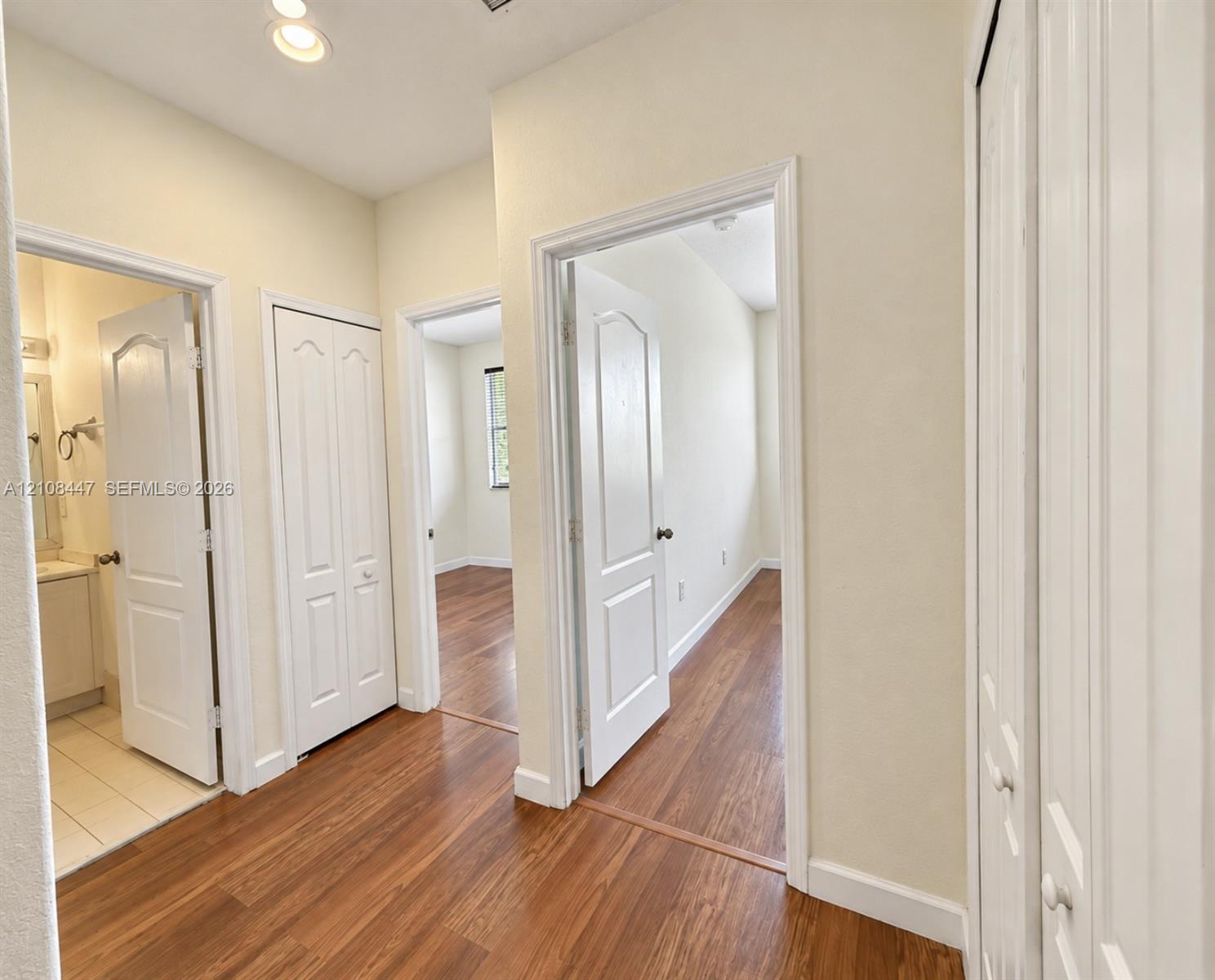 Hallway featuring wood-finish flooring, white paneled interior doors, and multiple built-in closets with bi-fold doors