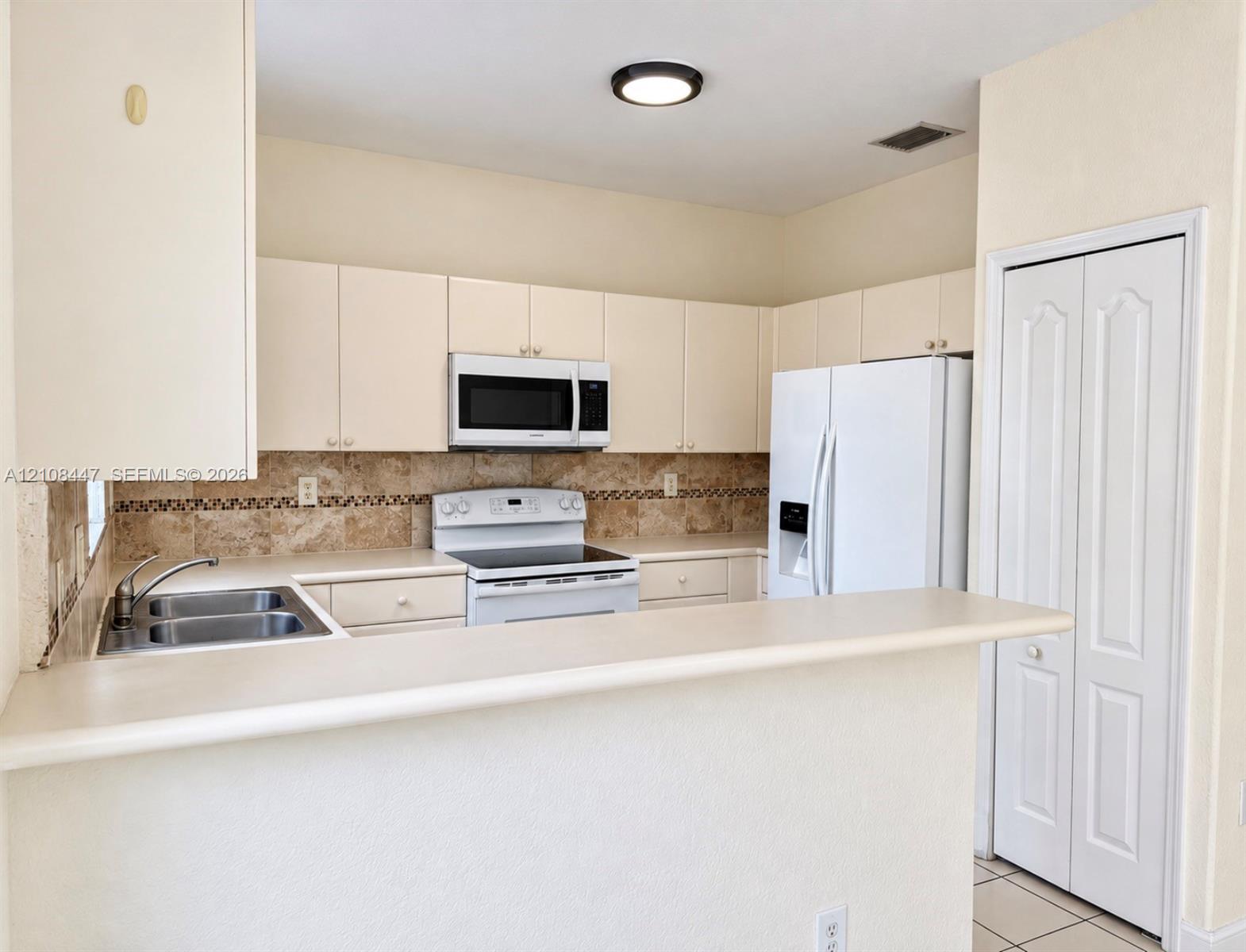Kitchen featuring light-toned cabinetry, solid surface breakfast bar, stone-finish backsplash, and white major appliances