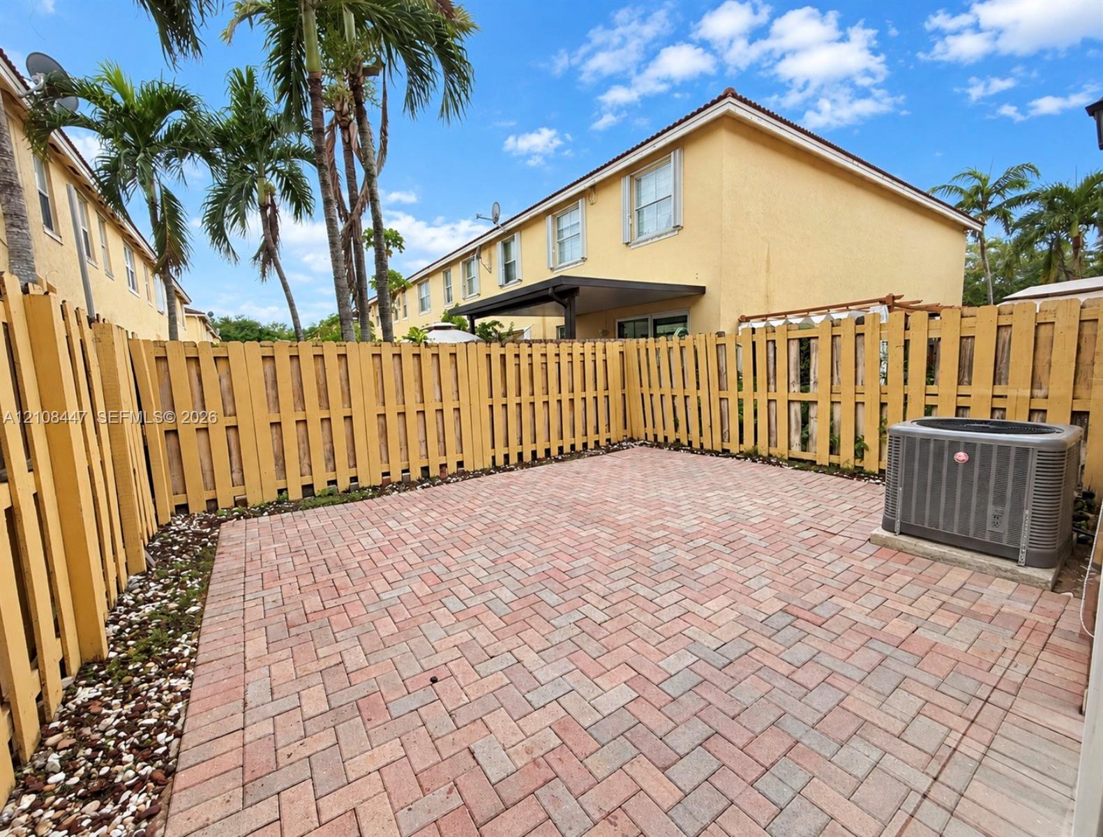 Enclosed courtyard featuring a herringbone brick paver patio, tall wood-style privacy fencing, and exterior stucco siding