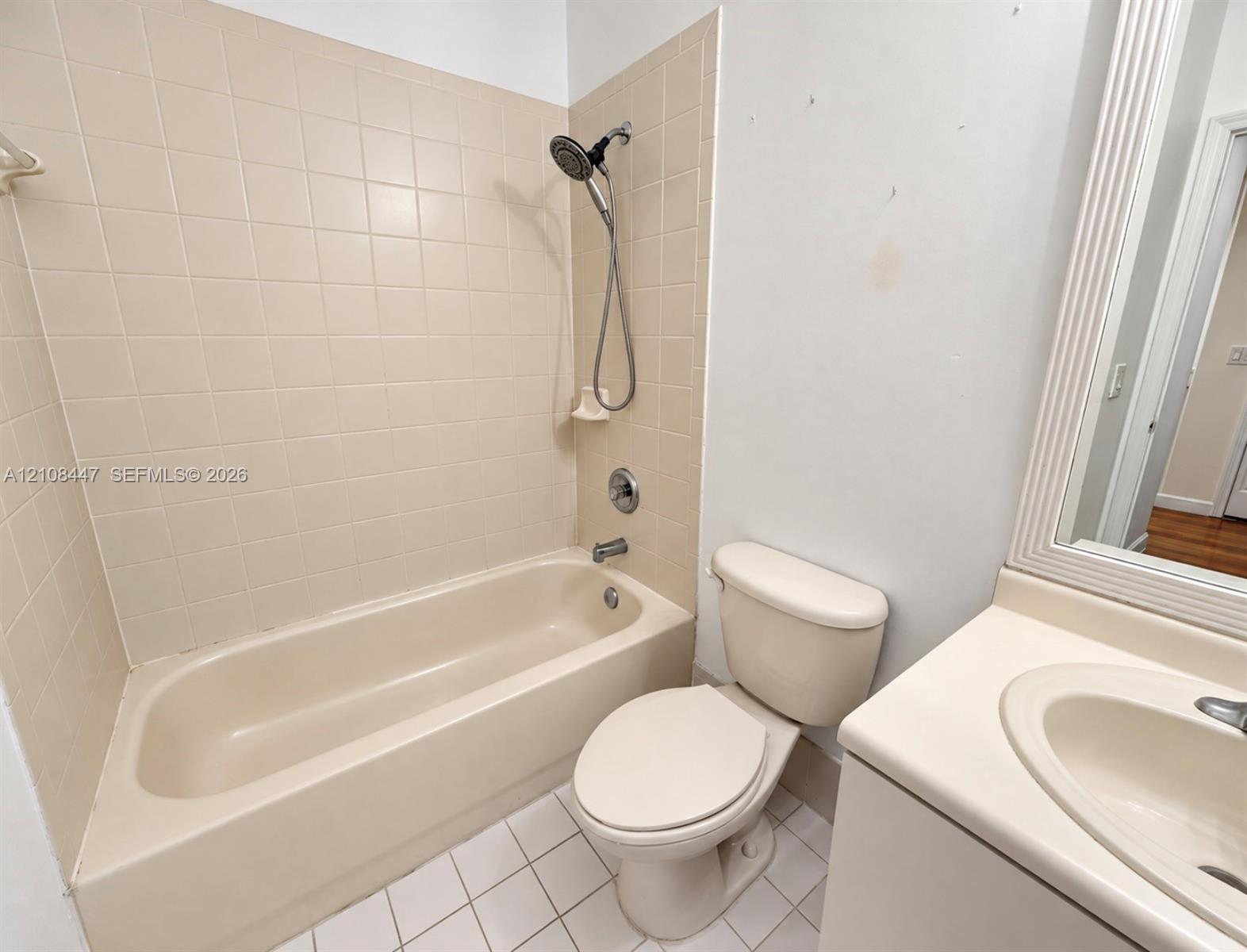 Full bathroom featuring a tub-shower combination with ceramic tile surround, a porcelain toilet, and a vanity with an integrated basin and framed wall mirror