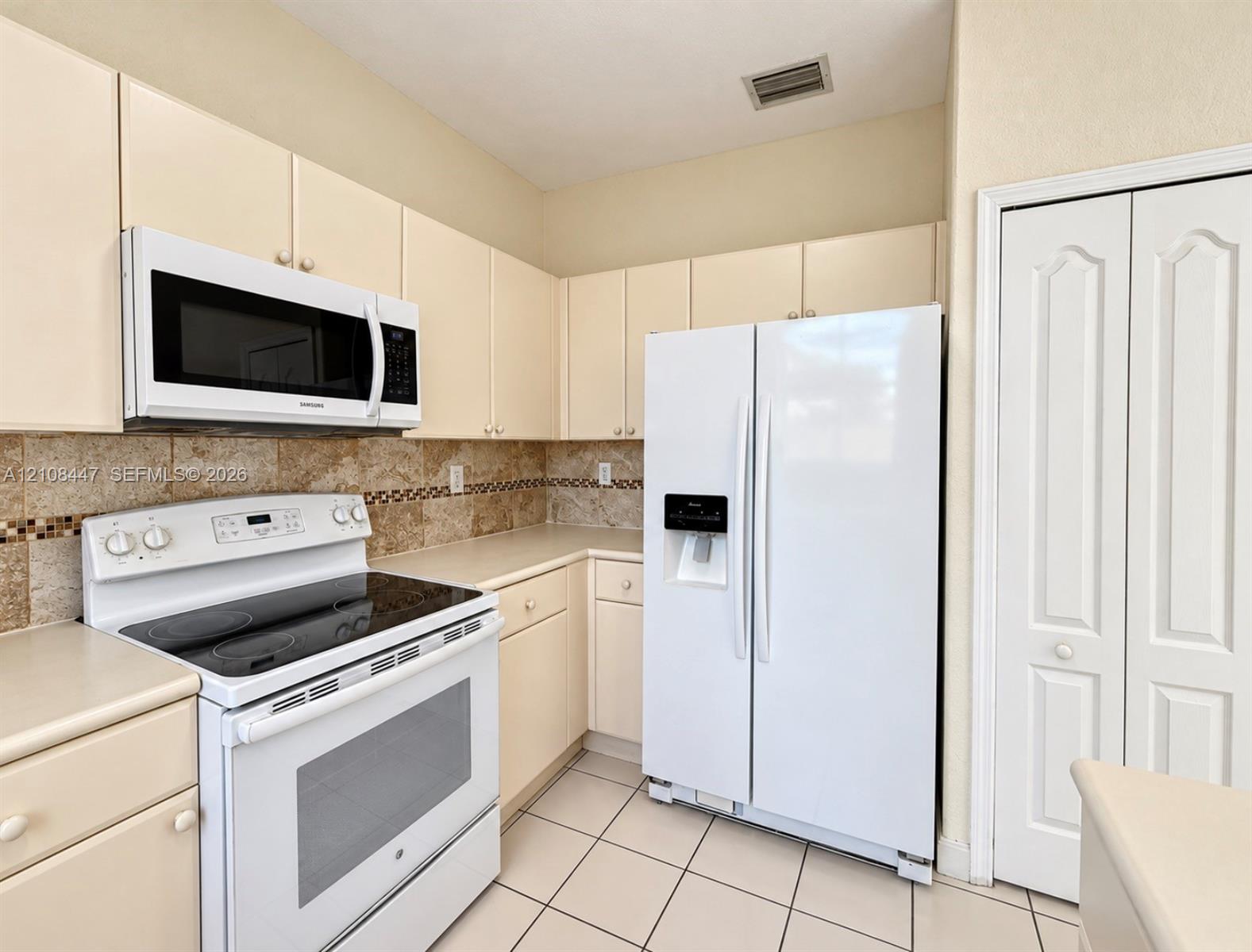 Kitchen featuring solid-surface countertops, stone tile backsplash with decorative inlay, white appliances, and light-toned cabinetry