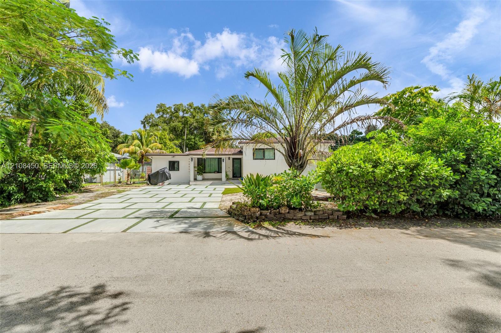 Single-story residence featuring a structured paver driveway with integrated grass joints, a covered entryway, and mature tropical landscaping