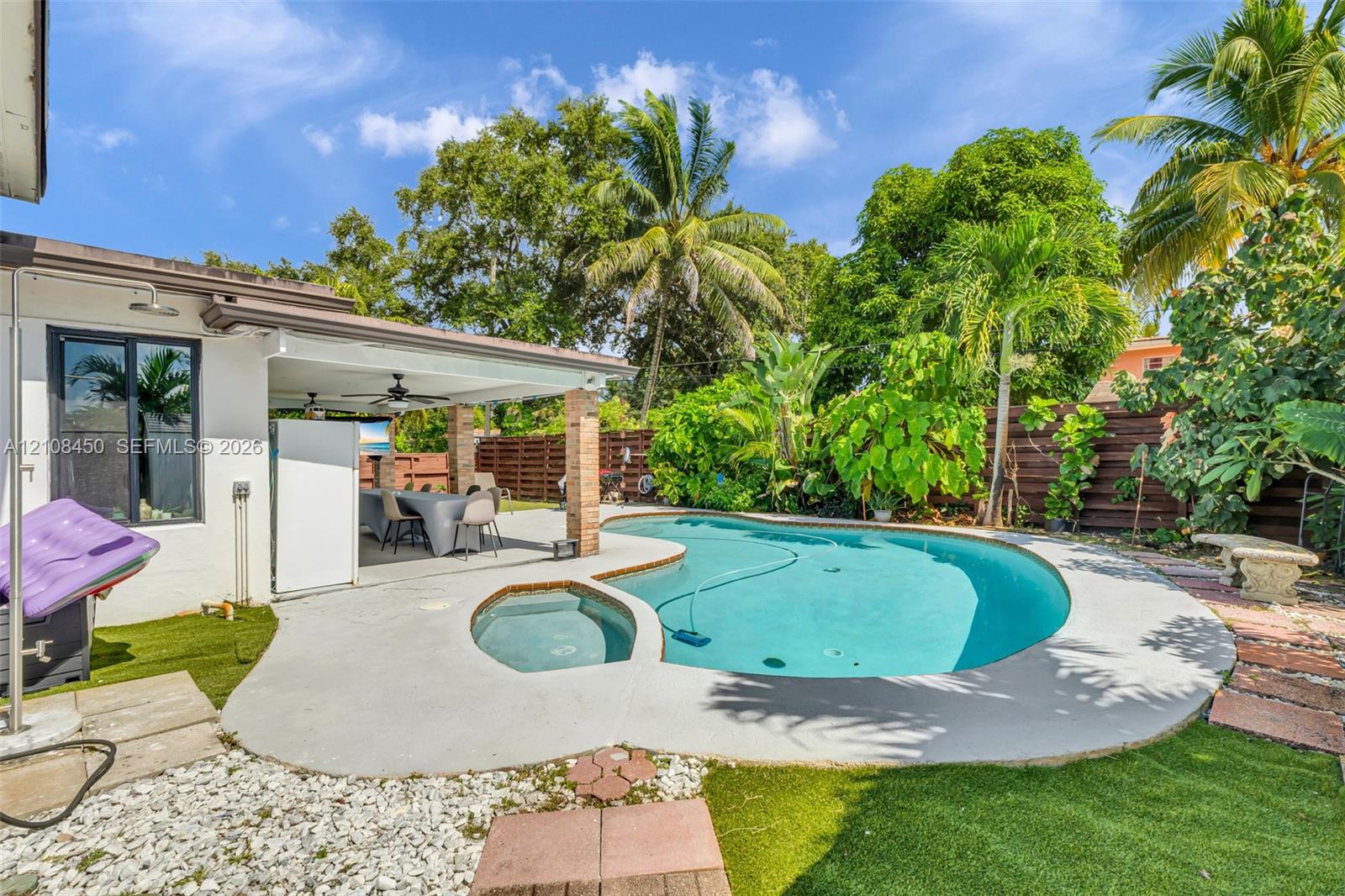 Backyard featuring a custom-shaped swimming pool with integrated spa, concrete patio, covered lanai with ceiling fans, and wood-slat privacy fencing