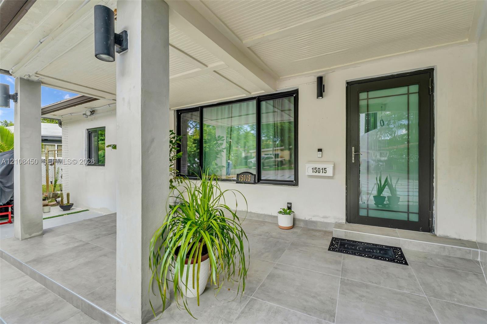 Covered entryway featuring large-format gray tile flooring, a glass-panel entry door, and dark-finished exterior cylindrical wall sconces