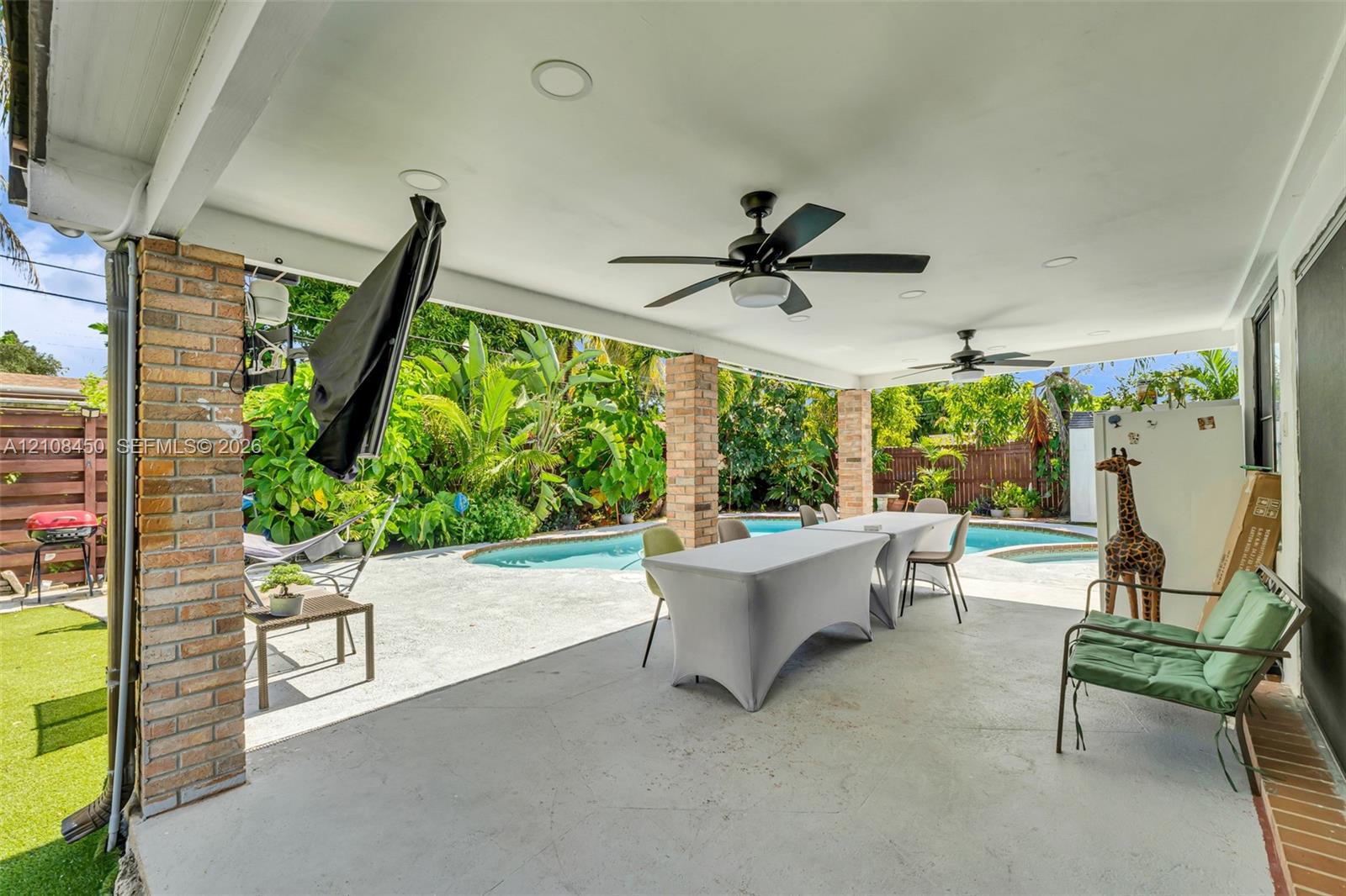 Covered patio featuring brick support columns, recessed lighting, and dual ceiling fans, opening onto a concrete pool deck with an inground pool