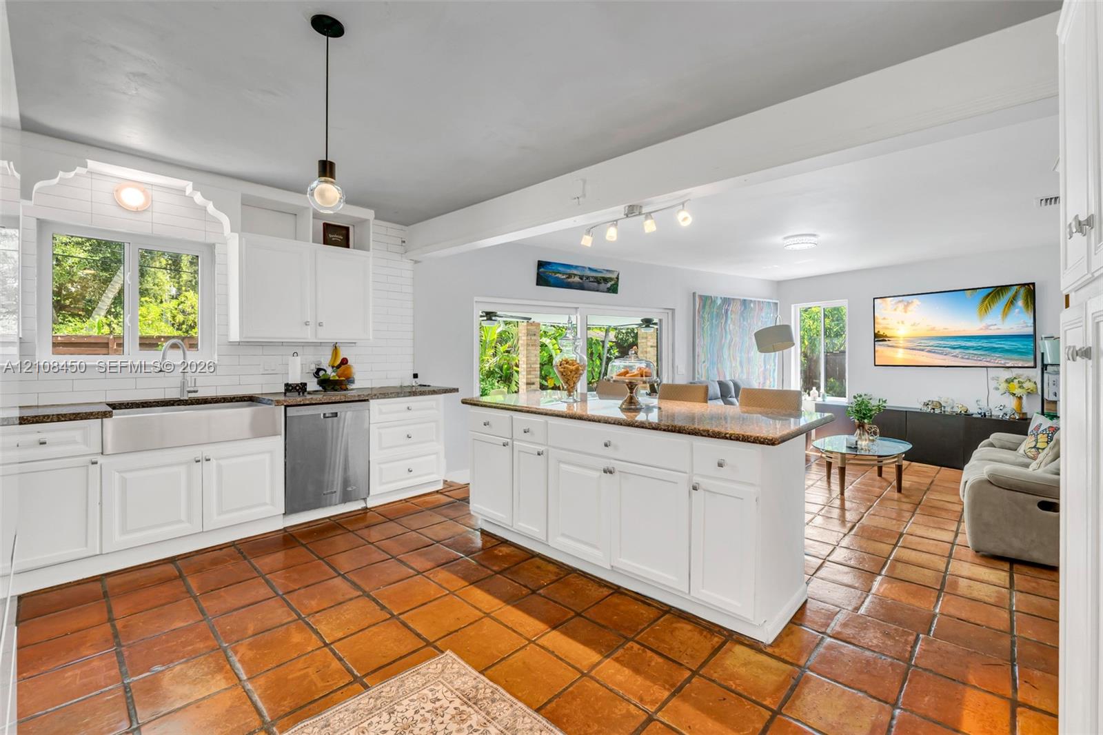 Kitchen featuring white cabinetry, a farmhouse-style stainless steel apron sink, a central island with a stone-finish countertop, white subway tile backsplash, and terracotta tile flooring