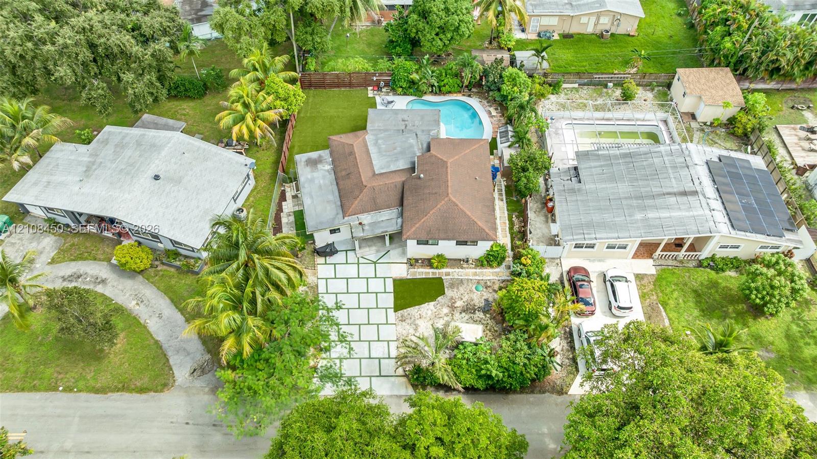 Aerial perspective of a property featuring a multi-pitched roof, paver driveway, swimming pool, and manicured lawn