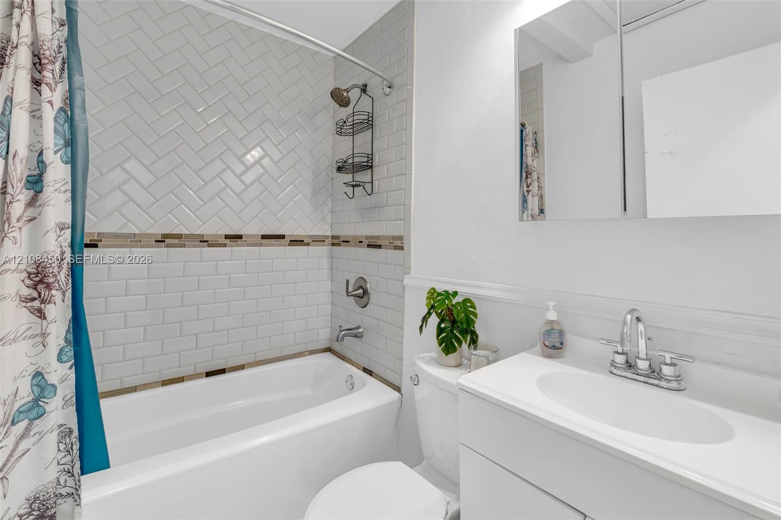 Full bathroom featuring a tub-shower combination with herringbone and subway tile surround, integrated vanity with an oval basin, and a mirrored medicine cabinet