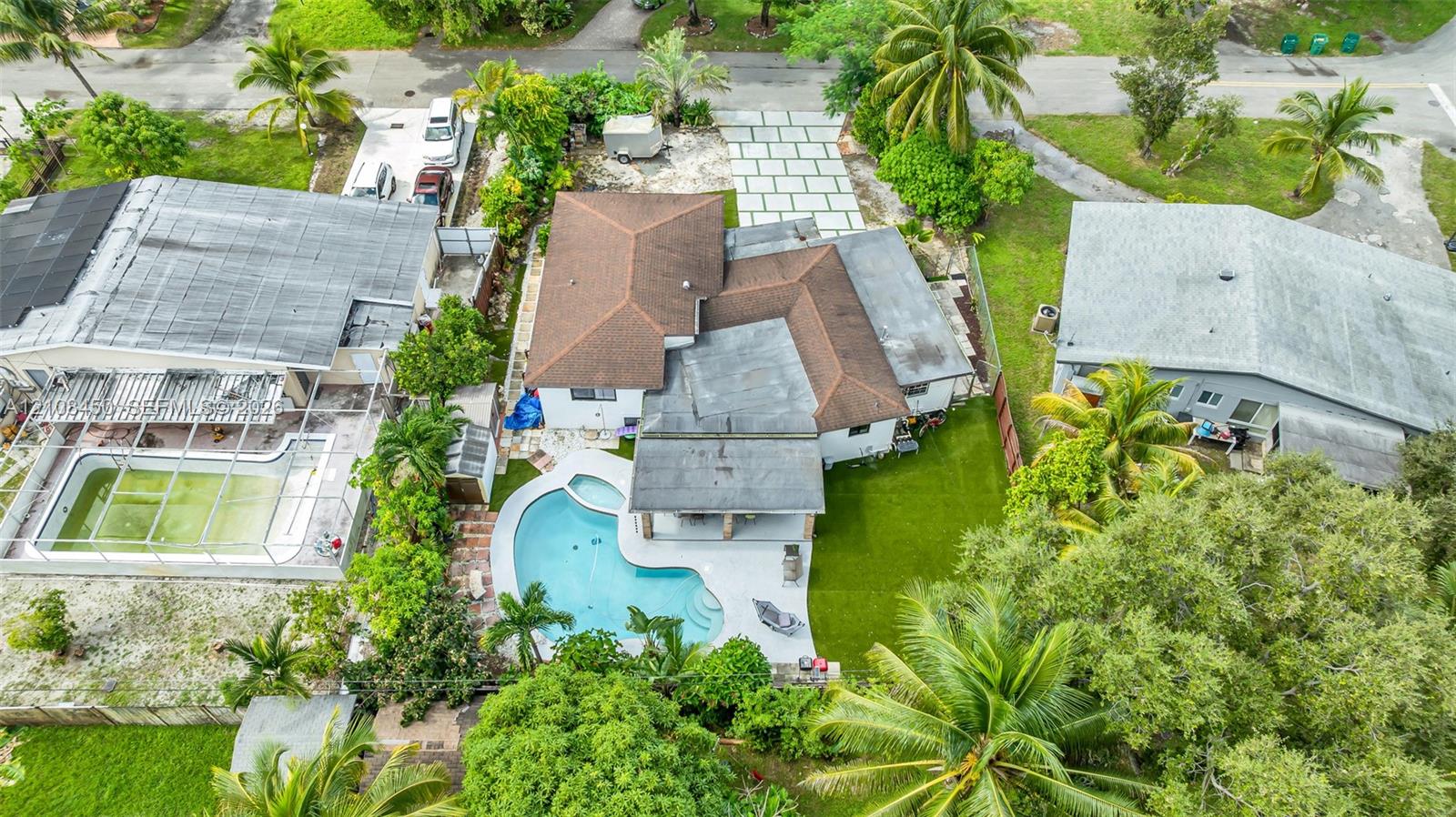 Aerial perspective featuring a shingle-roof residence with a backyard swimming pool, concrete hardscaping, synthetic turf lawn, and a paved driveway