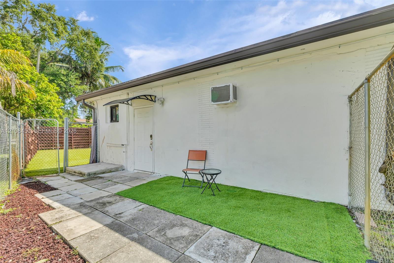 Exterior space featuring painted masonry walls, concrete paver patio, synthetic turf area, and chain-link perimeter fencing