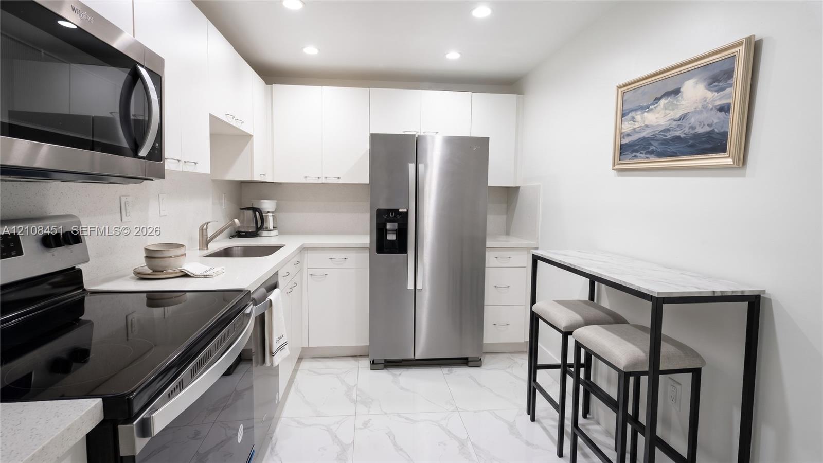 Kitchen featuring white flat-panel cabinetry, stainless steel appliances, solid surface countertops, and white tile flooring with grey veining