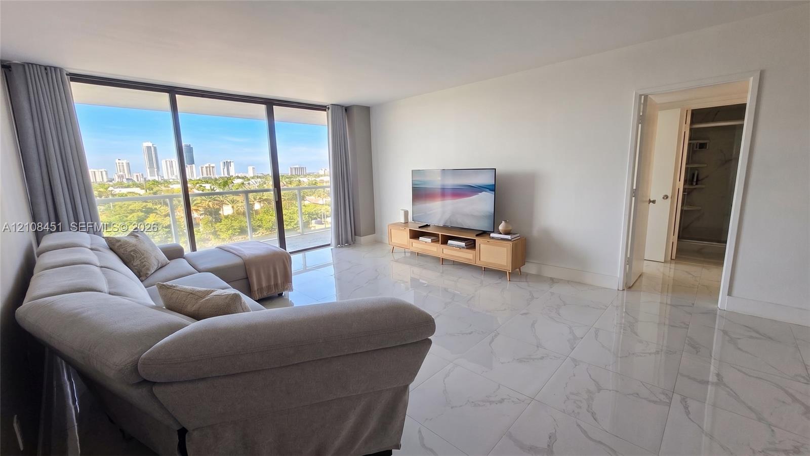 Living area featuring large-format tile flooring, floor-to-ceiling glass sliding doors, and a private balcony with an expansive cityscape