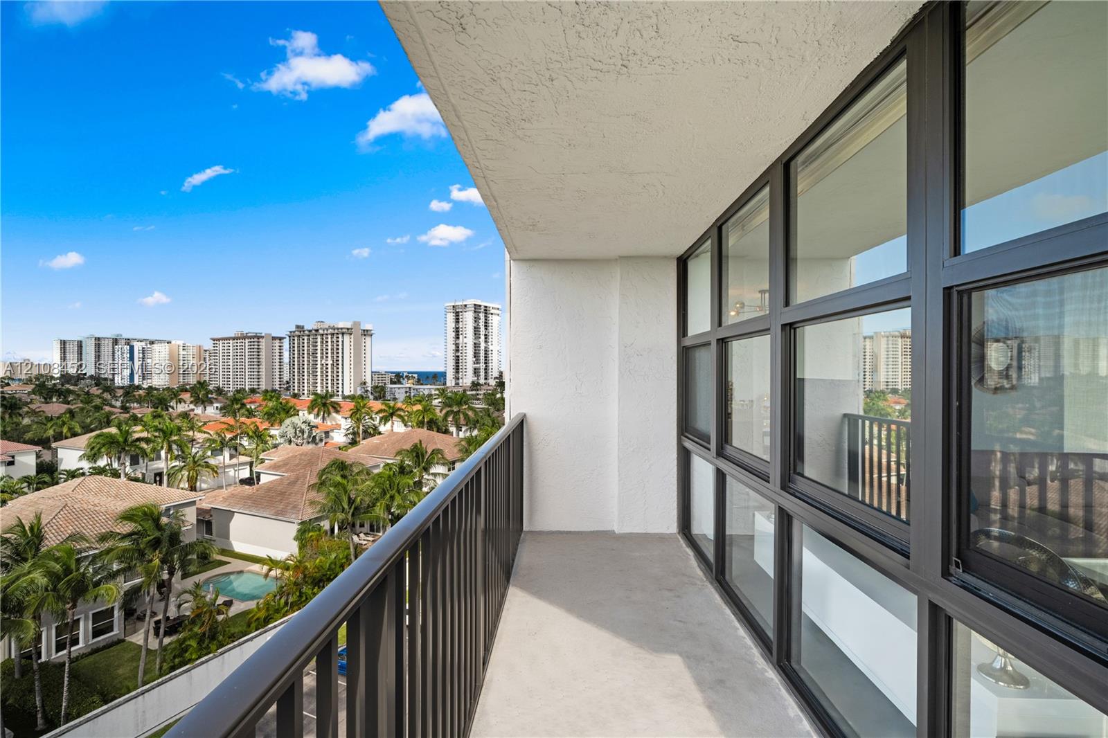 Covered balcony featuring metal railing, concrete flooring, and extensive glass window wall with dark framing