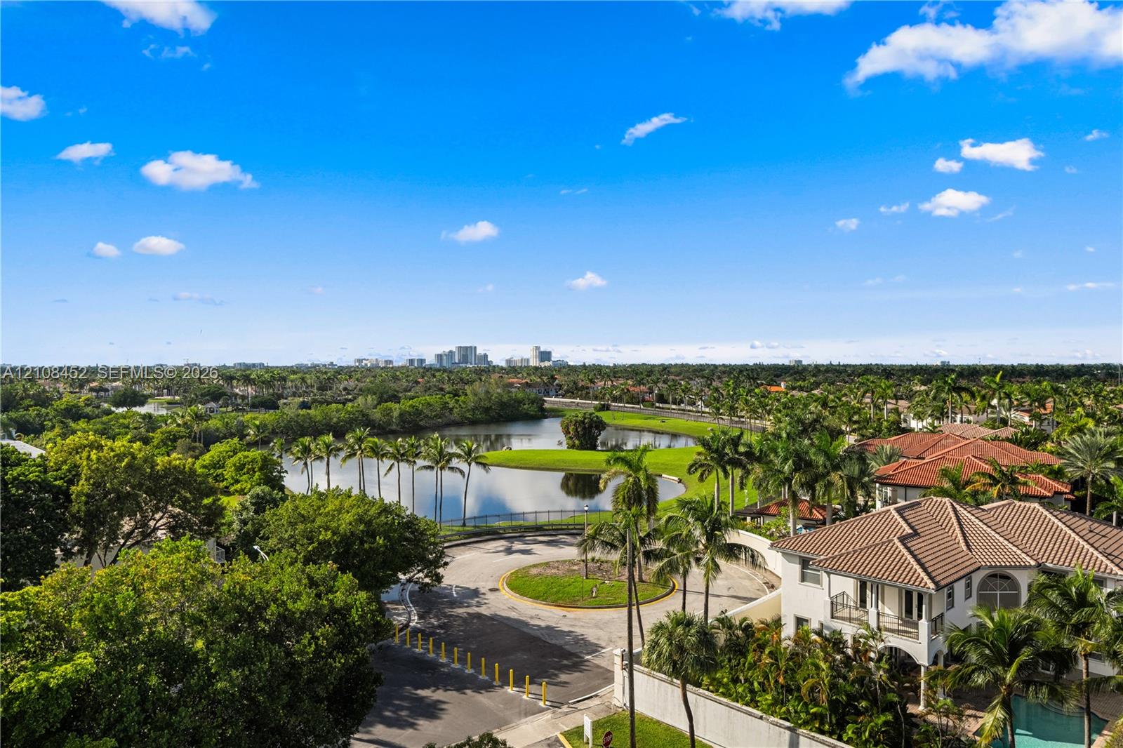 Aerial perspective featuring a tiled-roof residence, expansive water feature, mature palm trees, and panoramic cityscape horizon