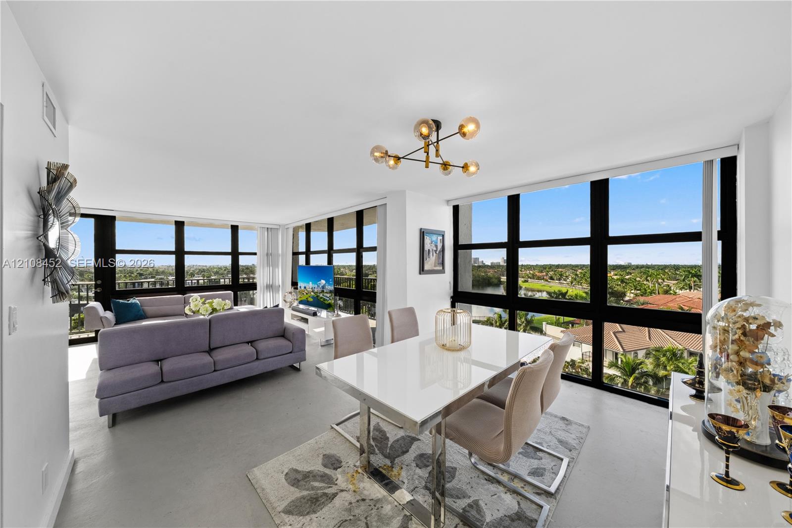 Open-concept living space featuring floor-to-ceiling windows, uniform light-toned flooring, and a multi-arm geometric ceiling fixture