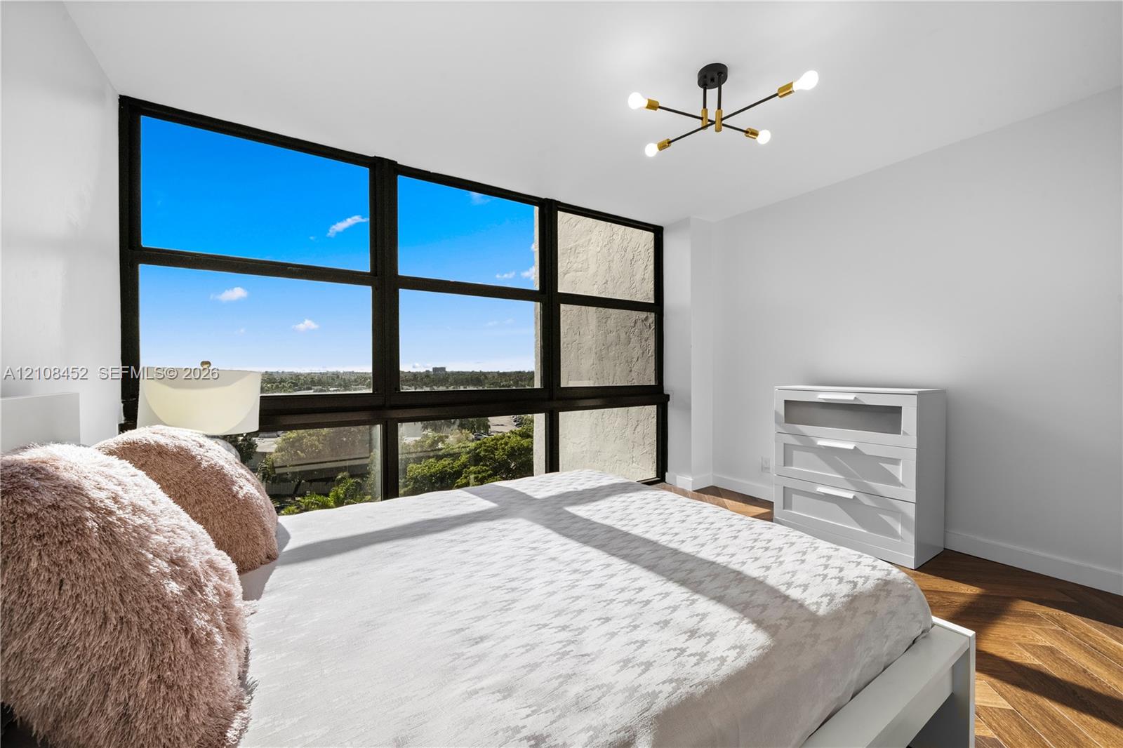 Floor-to-ceiling windows with black frames, wood-finish herringbone flooring, and a multi-arm sputnik-style ceiling light fixture