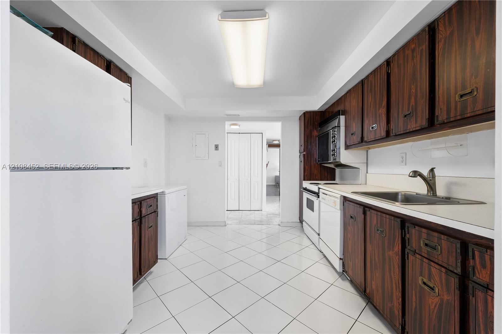 Kitchen featuring wood-finish cabinetry, white tile flooring, integrated white appliances, and a stainless steel sink with a high-arch faucet