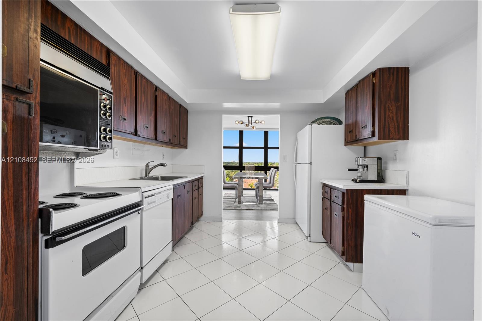 Kitchen featuring wood-finish cabinetry, white tile flooring, integrated white appliances, and a rectangular ceiling-mounted light fixture