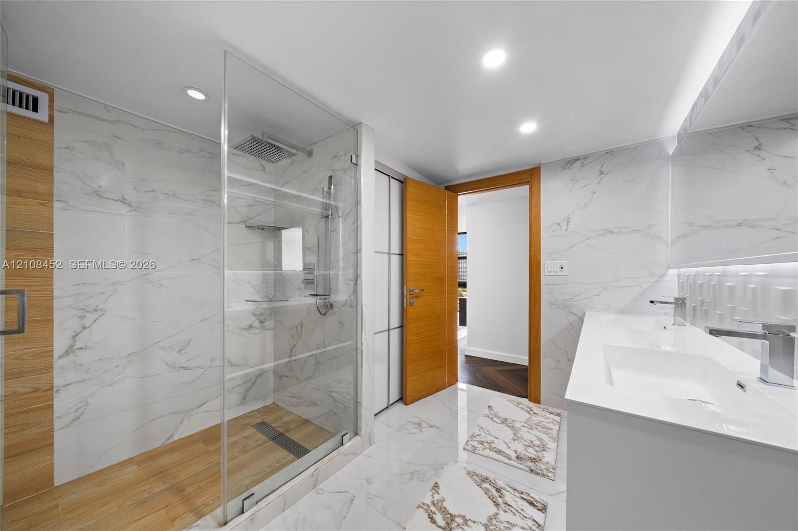 Walk-in shower with a glass enclosure, wood-finish flooring, and wall-mounted rain shower head