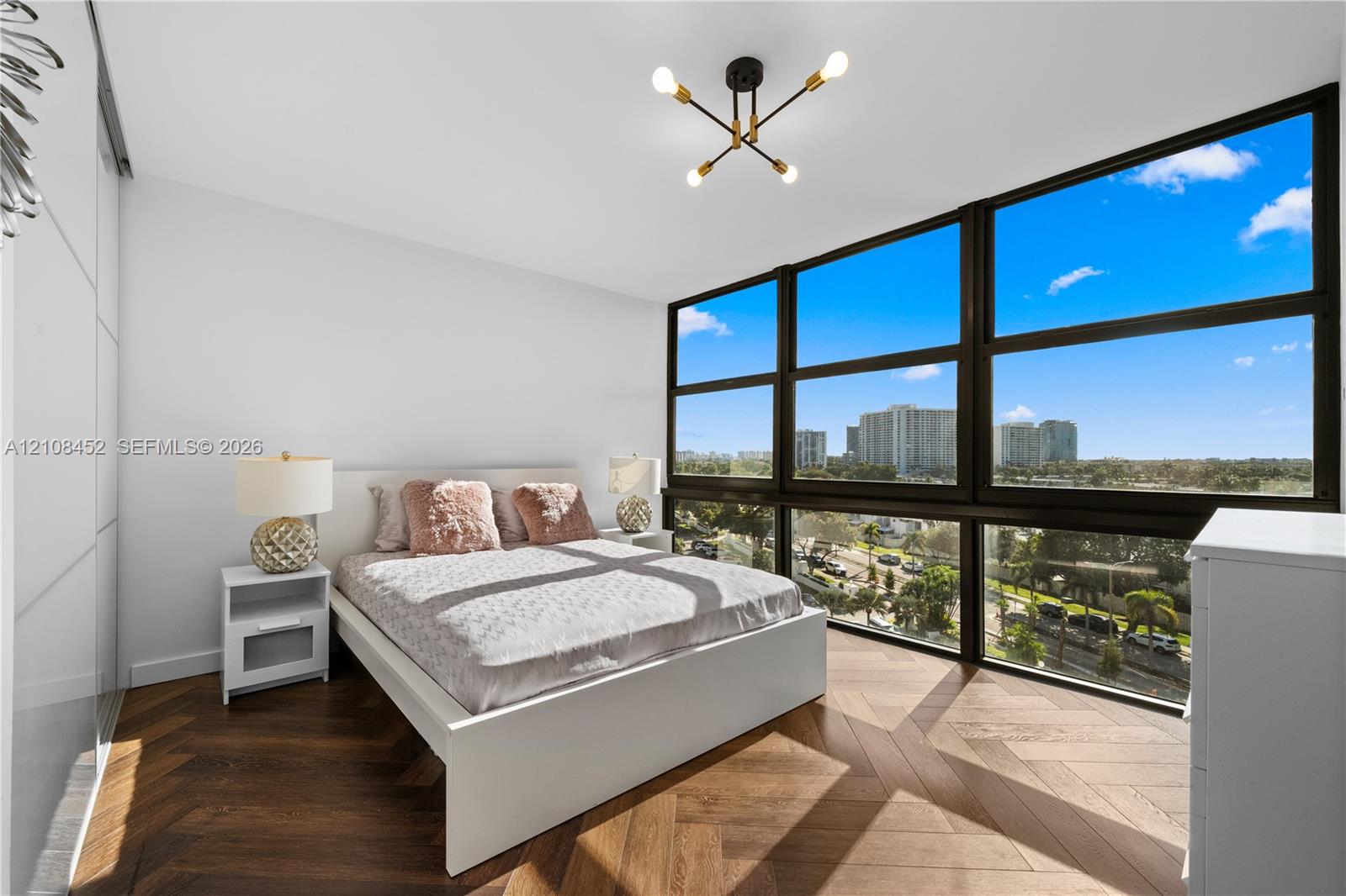 Floor-to-ceiling windows, chevron-patterned wood-finish flooring, built-in panel-front wardrobe, and a multi-arm geometric ceiling fixture