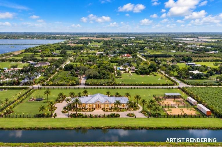 Aerial view of a sprawling estate featuring a multi-gabled roofline, extensive manicured grounds, a circular paved motor court, dual equestrian-style fenced arenas, and waterfront canal frontage