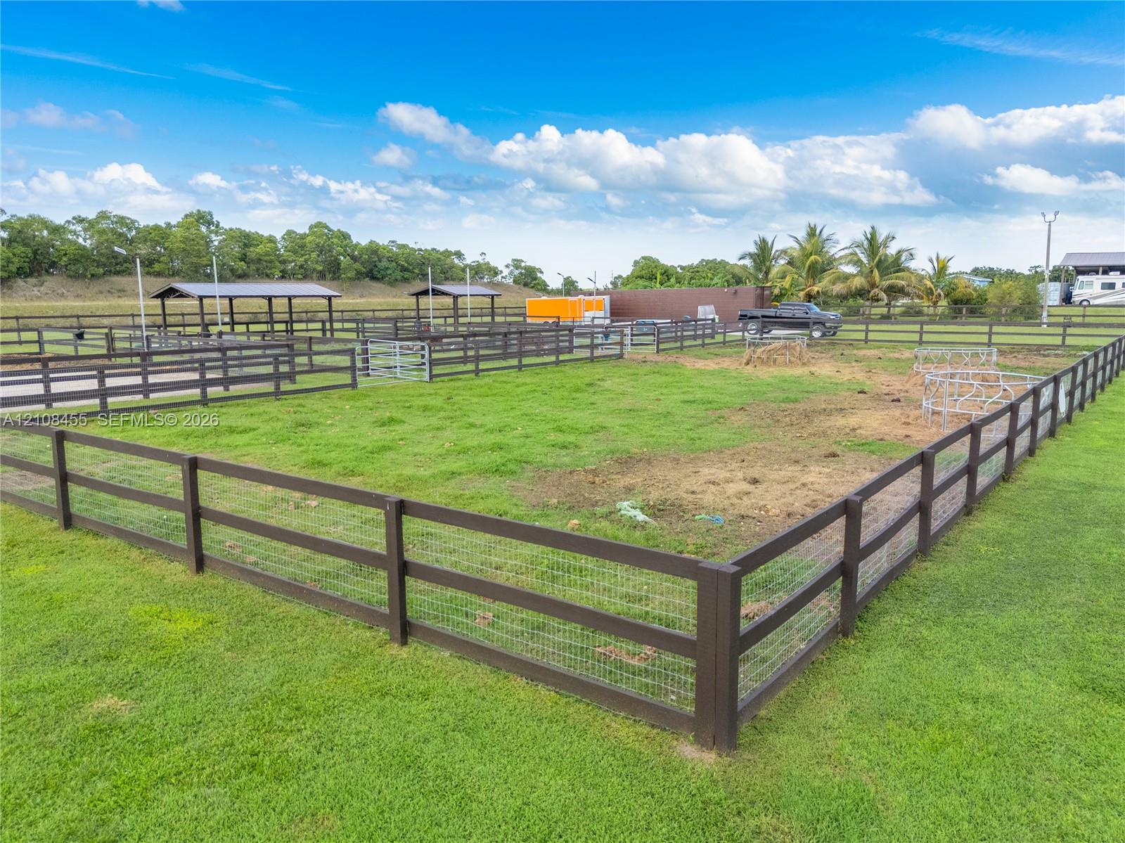 Fenced pasture area featuring multiple paddocks, metal roofing structures, and wire-mesh perimeter fencing