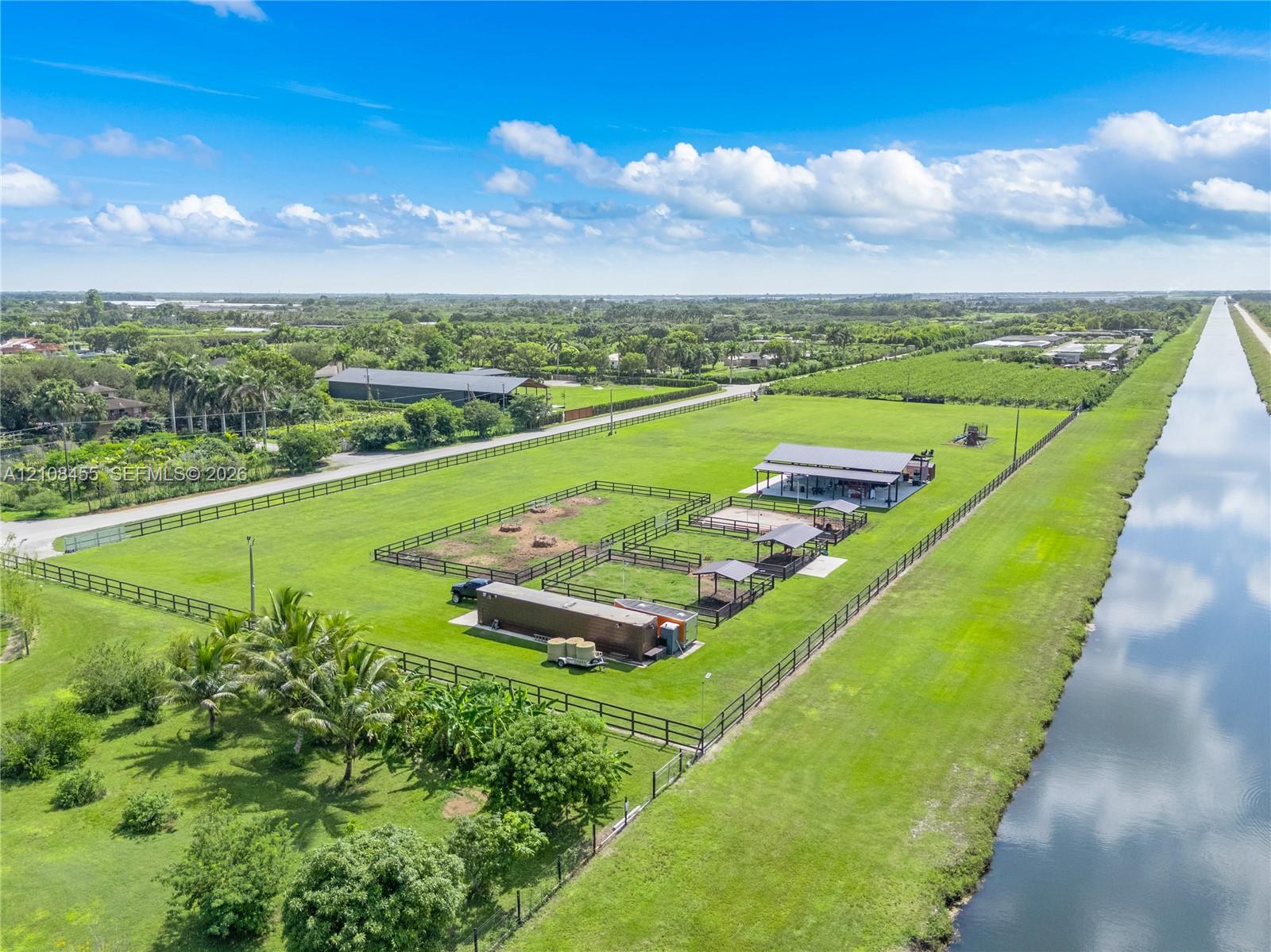Expansive grounds featuring perimeter fencing, multiple structured paddocks, covered outdoor stalls, and a metal-roofed barn structure