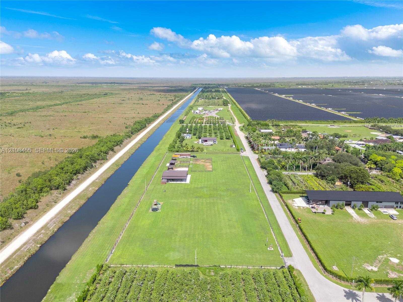 Expansive acreage featuring level pasture land, perimeter fencing, multiple detached metal structures, and direct water frontage