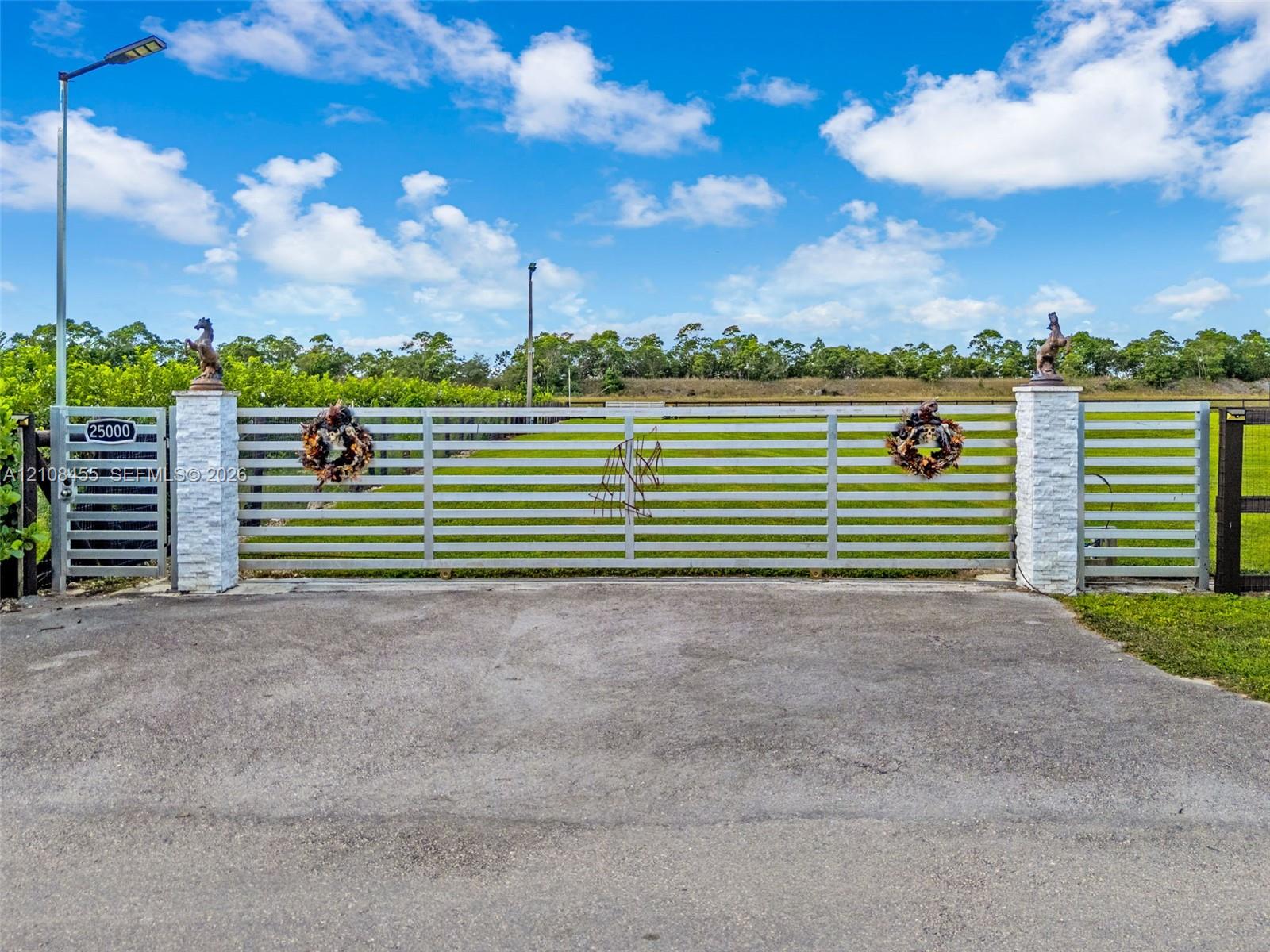 Gated entry featuring a horizontal-slat metal gate, stacked stone pillars, and an asphalt driveway