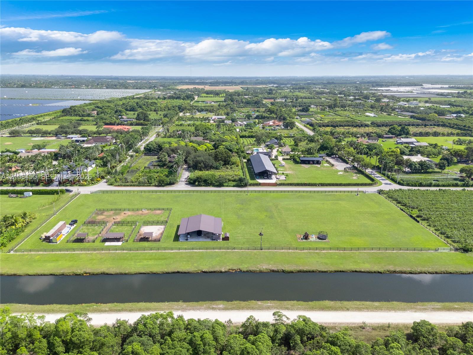 Expansive acreage featuring a metal-roof barn, perimeter fencing, designated equestrian stalls, and a water frontage boundary