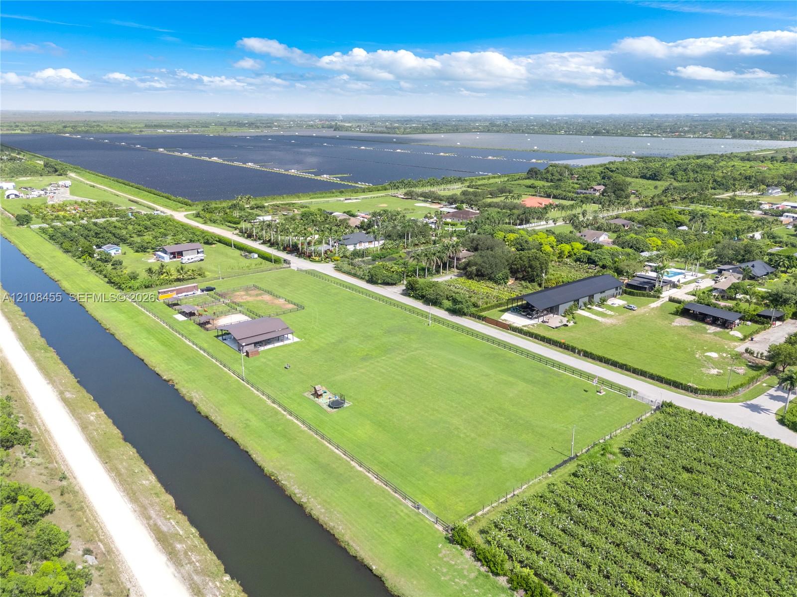 Aerial perspective featuring an expansive grass parcel, border canal, perimeter fencing, and mature vegetation