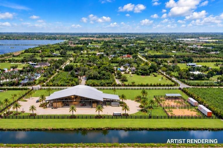 Aerial view of a sprawling property featuring a large open-air pavilion with metal roofing, perimeter fencing, multiple fenced-in sand areas, and direct waterfront access