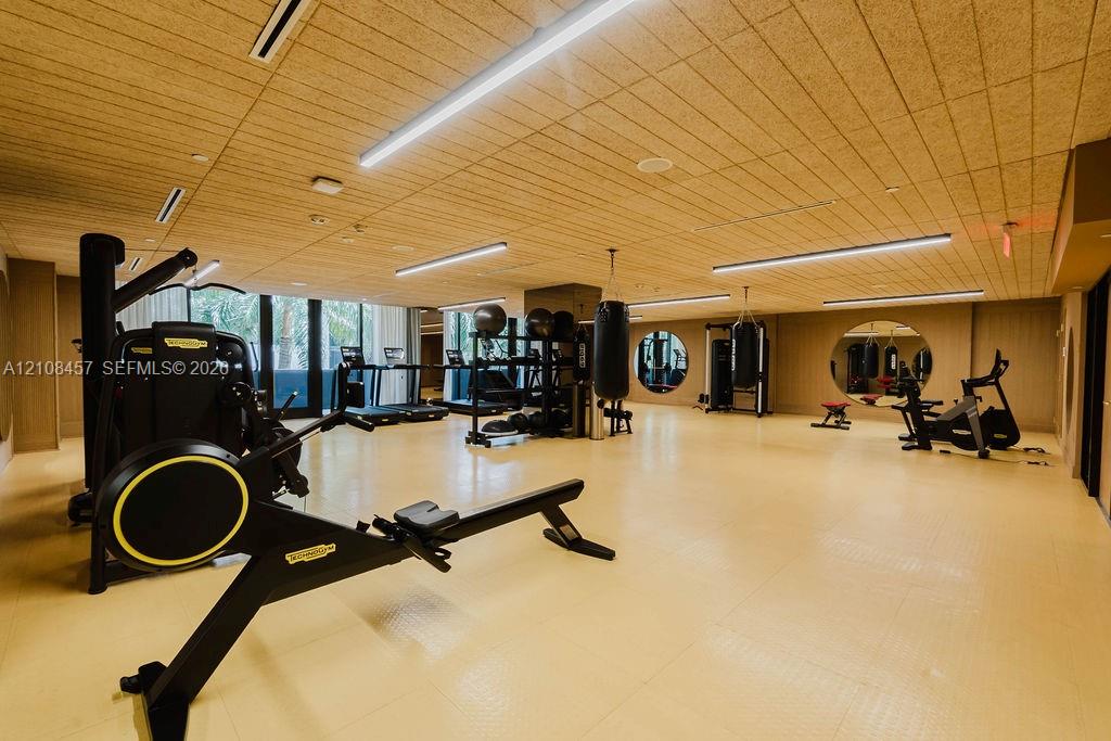 Spacious fitness room featuring wood-slat ceiling, recessed linear lighting, circular wall mirrors, and textured resilient flooring