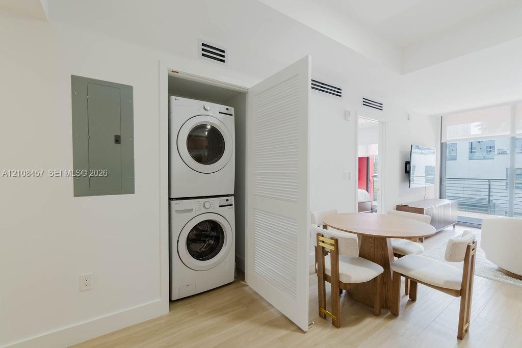 Stacked laundry center featuring a high-efficiency front-load washer and dryer enclosed by a louvered door, wood-finish flooring, and minimalist white interior walls