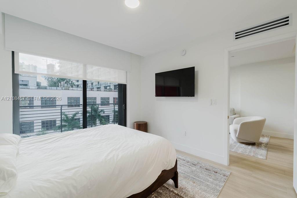 Floor-to-ceiling windows featuring automated roller shades, wood-finish flooring, and a private balcony with horizontal metal railing