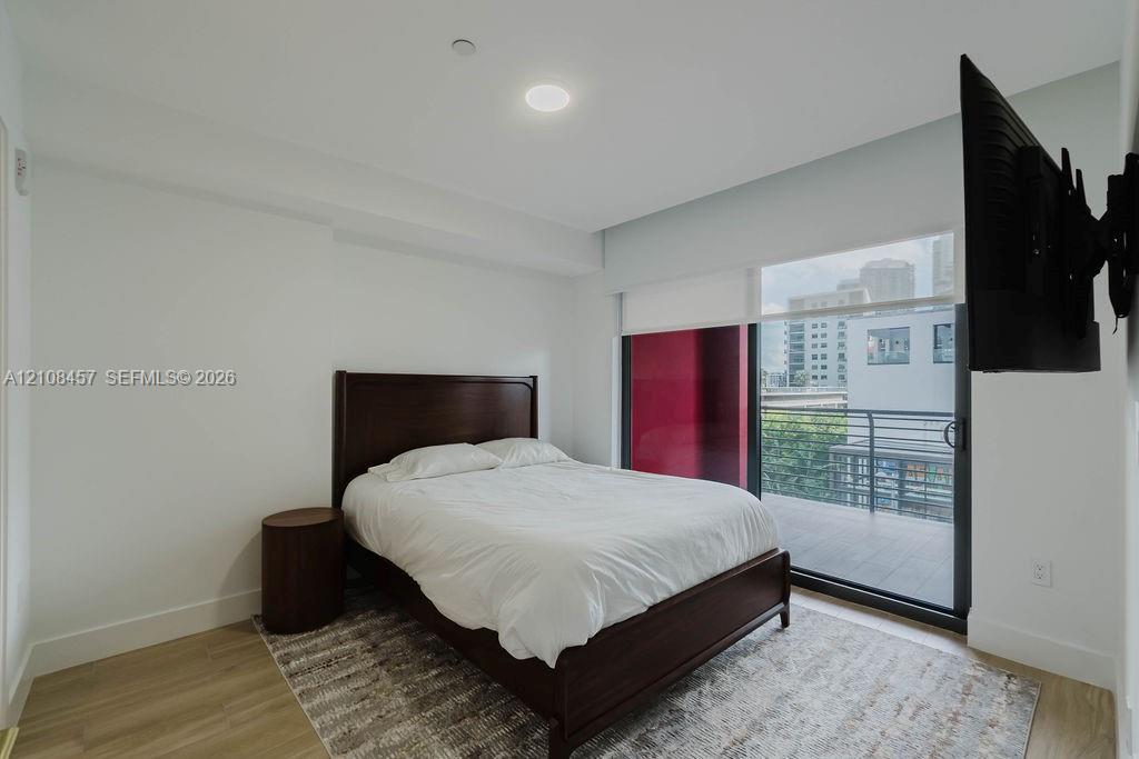 Sliding glass door opening to a private balcony with metal railing, neutral wood-finish flooring, and recessed ceiling lighting