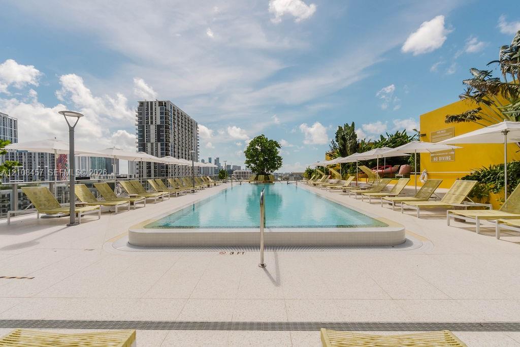 Rooftop swimming pool featuring a tiled deck, metal handrail, and integrated landscaping