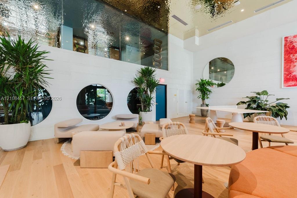 Expansive common area featuring high ceilings with a metallic finish, light wood-finish flooring, circular windows, and a large round wall mirror