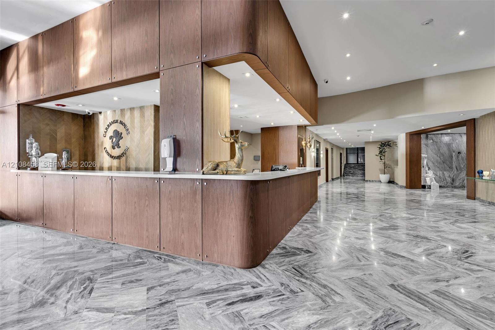 Lobby area featuring polished natural stone flooring in a herringbone pattern, wood-panelled custom reception desk with a solid surface countertop, and recessed ceiling lighting
