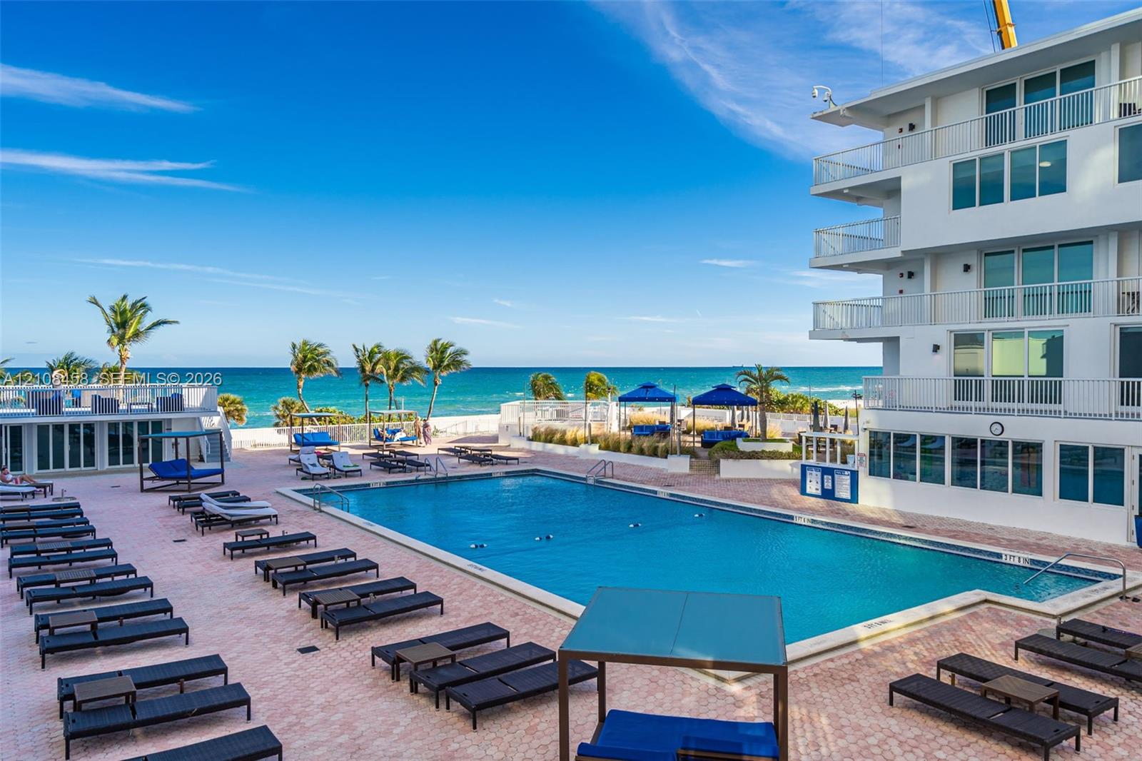 In-ground rectangular swimming pool surrounded by a brick paver deck, multi-story building with private railed balconies, and direct oceanfront access